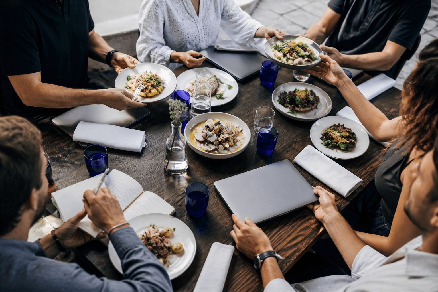 Shared lunch plates and laptops around a dark wooden table